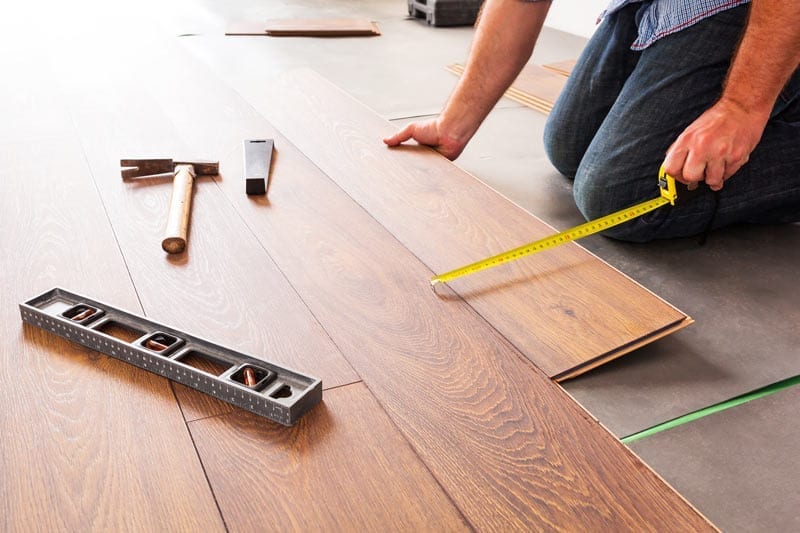 Worker measures hardwood flooring during installation